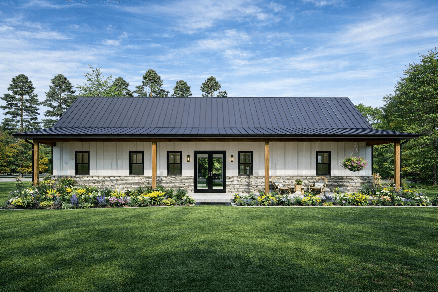 Modern white farmhouse with black metal roof, stone accents, and lush, colorful flower gardens.